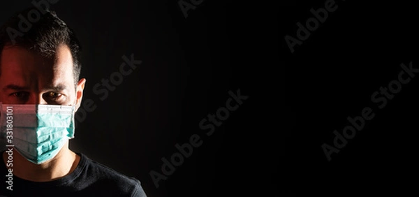 Fototapeta Portrait of a young man with a medical mask on a black background. Protect your health. Concept of Coronavirus