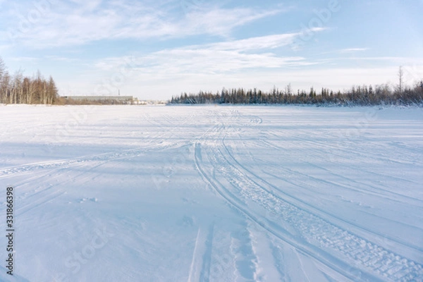 Fototapeta a large empty area covered with snow and snowmobile tracks. A guy in a yellow jacket rides a snowmobile