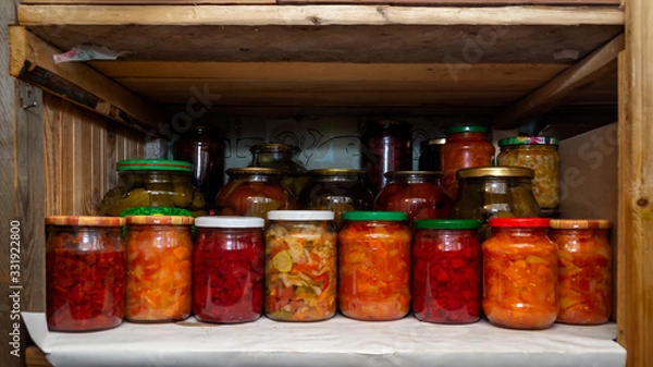 Fototapeta Wooden shelf in pantry with provisions in glass jars with pickled vegetables