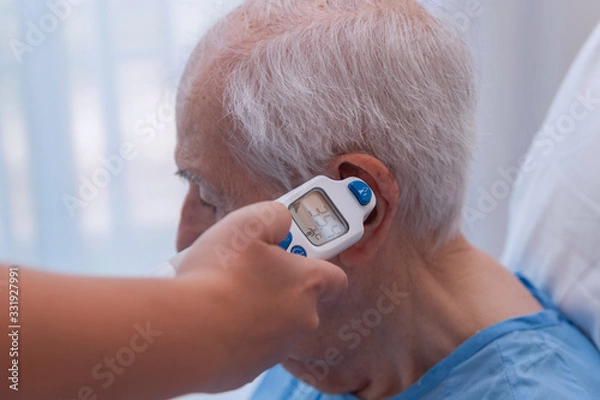 Fototapeta Close-up of a nurse taking an elderly man's temperature with a digital thermometer in her ear