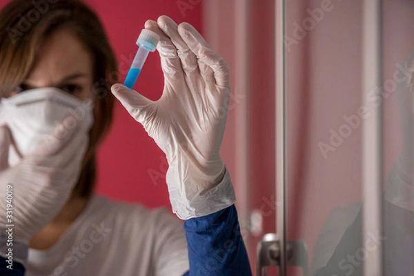 Fototapeta nurse wearing white surgical gloves and holding molded mask while examining a test tube with coronavirus flu vaccine in the medical laboratory to study a cure to stop the pandemic in the world