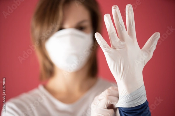 Fototapeta nurse with molded mask puts on surgical gloves to prevent coronavirus infections and prevent the spread of the world pandemic