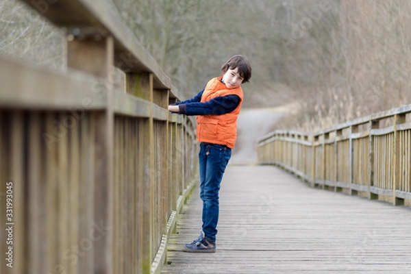 Fototapeta Portrait of a handsome boy standing on a wooden bridge.