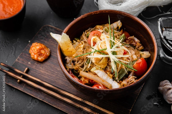 Fototapeta Chinese dishes in a clay plate on a black concrete background with ingredients for delivery