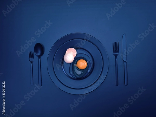 Fototapeta Blue dishes with a broken egg and shell on a plate. Ceramic dishes with a fork, spoon and knife. For cafes, posters, breakfasts and dinners. Copyspace for your individual text