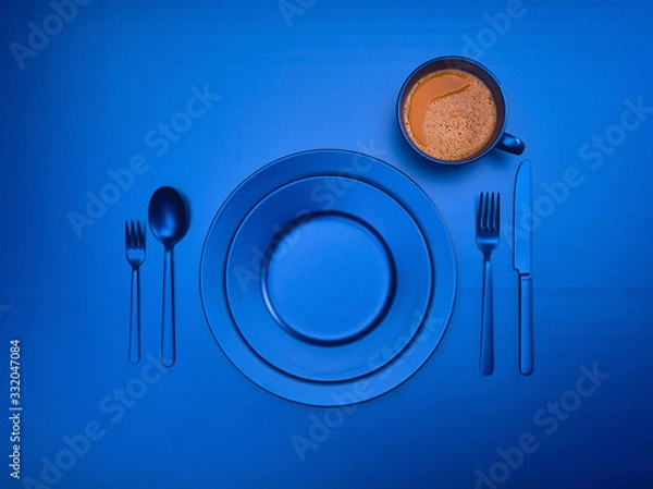 Fototapeta Cup of coffee with blue plates, fork, knife and spoon, top view. Ceramic dishes with a set of cutlery. Empty blue dishes for breakfast or dinner in a restaurant. Copyspace for your individual text.