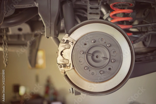 Fototapeta  car brake part at garage,car brake disc without wheels.Disk brake and car disk brake system service concept - Car disk brake pad replacement service by hand of mechanic man in car garage.Close up.