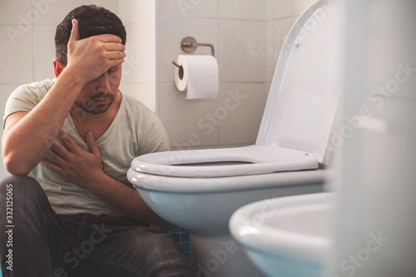 Fototapeta Man feeling bad putting his head in toillet and vomiting.