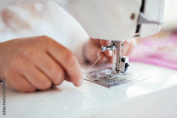 Obraz Seamstress puts a thread on a needle in a sewing machine