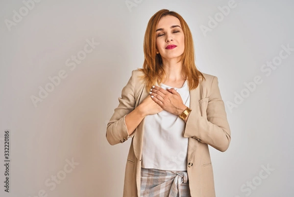 Fototapeta Redhead caucasian business woman standing over isolated background smiling with hands on chest with closed eyes and grateful gesture on face. Health concept.