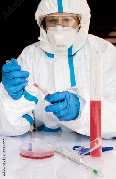 Fototapeta Laboratory technician performs tests to check contagion from Coronavirus Covid-19 completely covered by white overall, mask, gloves and glasses