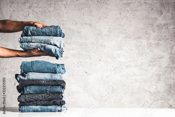 Fototapeta Hands, put the stack of blue jeans on gray background.