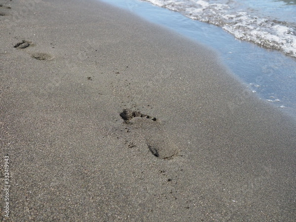 Fototapeta foot prints on a black sand beach with tilt-shift blur. Surf in background.