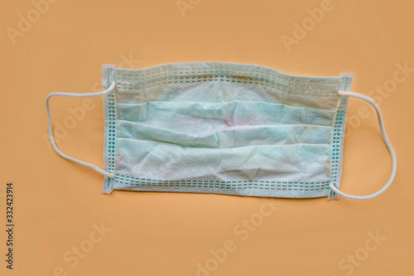 Fototapeta Used green surgical face mask with cosmetic stains, lipstick marks isolated on color background, cause of the spread of germs, virus or bacteria. problem of unhygienic disposal of infectious waste.