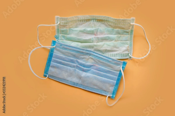 Fototapeta Used green surgical face masks with cosmetic stains, lipstick marks isolated on color background, cause of the spread of germs, virus or bacteria. problem of unhygienic disposal of infectious waste.