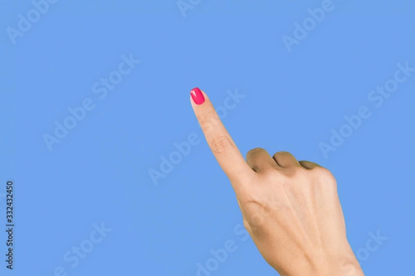 Fototapeta Closeup view photography of one manciured beautiful female hand making gesture by single index finger as if showing or pointing at something invisible isolated on blue background.