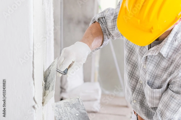 Fototapeta Builder using a trowel to add plaster to a wall