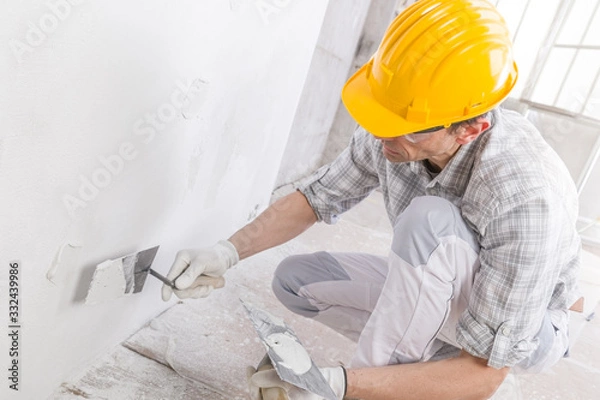 Fototapeta Builder using a trowel to add plaster to a wall