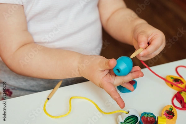 Fototapeta Child putting beads on a string. Bead stringing activity. Fine motor skills development. Lacing, threading.