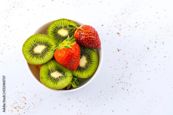 Fototapeta Sliced kiwis and strawberries in a white bowl with a white background with brown sugar
