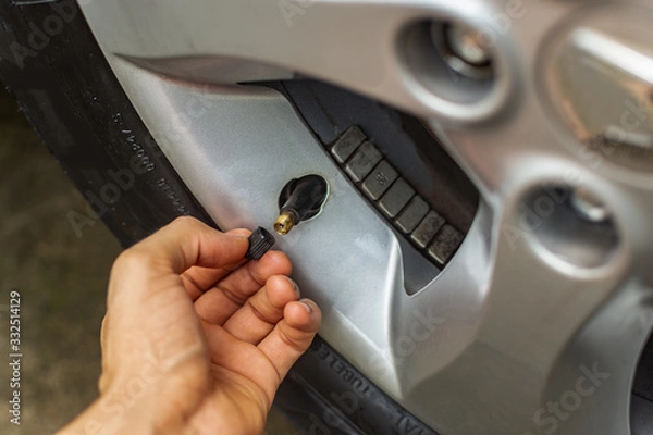 Fototapeta Temat problemów z samochodem. ręcznie umieszczając korek zaworu opony na c