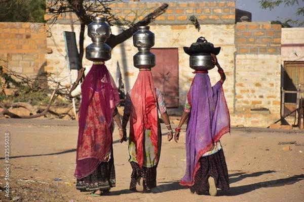 Obraz インドのラジャスタン州のジャイサルメール
クーリー村の砂漠地帯の道路を歩くインド人女性
民族衣装のサリーを着ている女性の姿
水瓶を頭に乗せて運ぶ３人組の後ろ姿