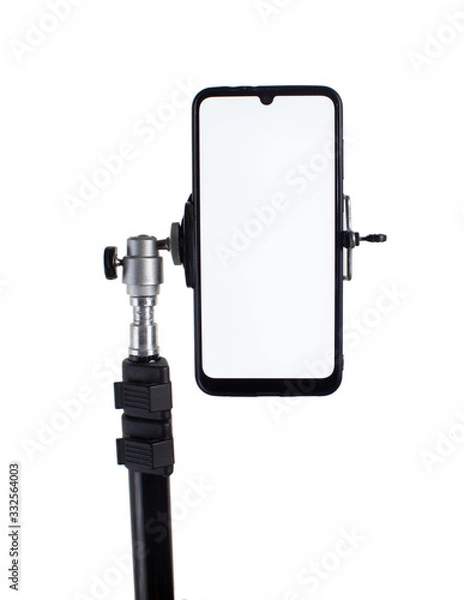Obraz Smartphone mounted on a black tripod in a vertical position on a light isolated background tilted to the right.