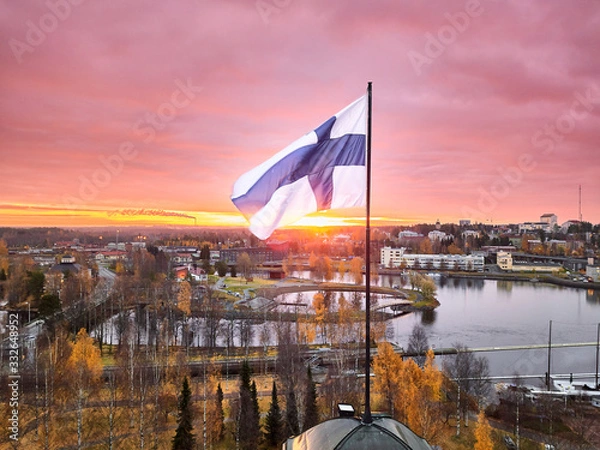 Fototapeta Aerial view of Finnish flag on the tower of Town Hall against the red sunrise sky in Joensuu, Finland.