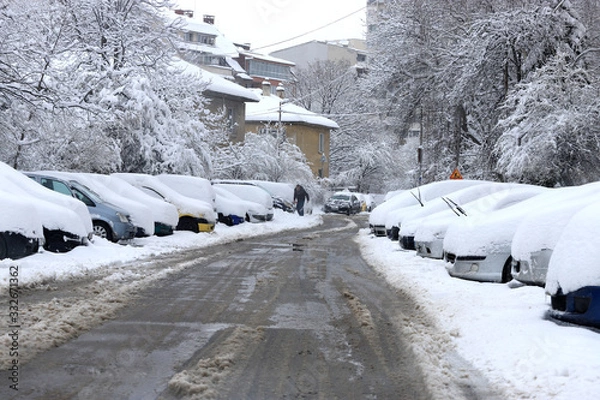 Fototapeta Uncleaned streets with heavy snowdrifts after snowfall in the city, cars under the snow.