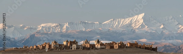 Fototapeta first morning sunlight falling on the cemetery of Terek, south of Baetov, near the Mels-Ashu pass with the amazing landscape of the  Tian Shan mountains covered in snow around