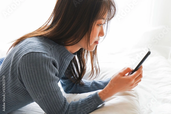 Fototapeta ベッドで寝る前にスマホを使う若い女性
