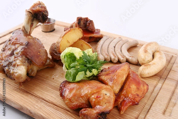 Fototapeta Dish of assorted meat. Big tasty baked  knuckle, homemade sausages, grilled bird, potatoes. With greens and sauces. On a wooden board.