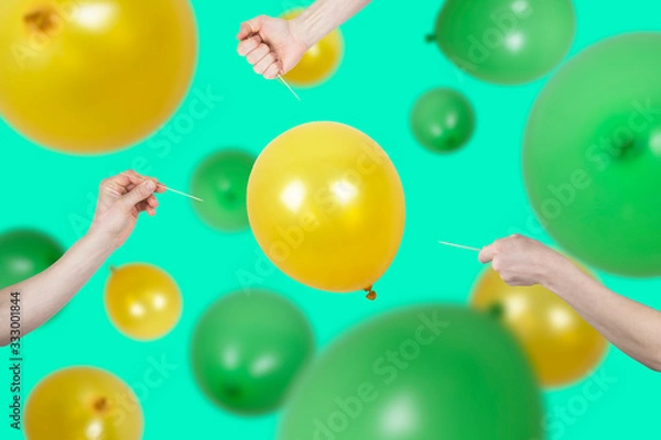 Fototapeta Danger concept of finance risk or goal targeting. Many cropped men hands hold needle directed to yellow air balloon in the middle out of focus green and yellow ballons in distance