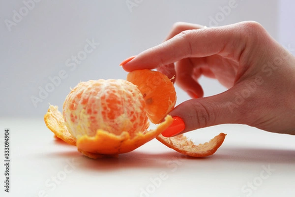 Obraz female hand with bright manicure holds a mandarin