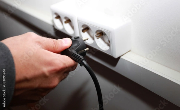 Obraz male hand sticks a plug into a socket