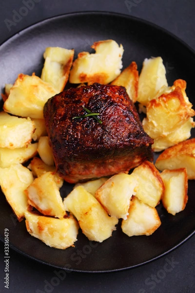 Fototapeta a piece of meat baked with potatoes on a black background