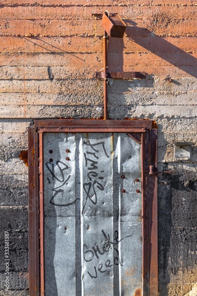 Obraz Natural texture of a beige cement wall and an iron rusty door aged by time with scuffs and moss in macro shot
