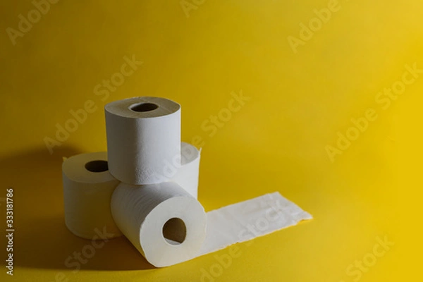 Fototapeta A stack of four white disposable toilet rolls on a bright yellow background. One roll lies untwisted. Soft fresh cotton. Essential goods. Purchasing power. Copy space. Drops a shadow from an object.