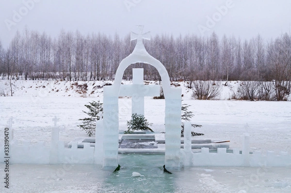 Fototapeta Cross carved from ice on a winter lake near the ice hole at Epiphany on a frosty day