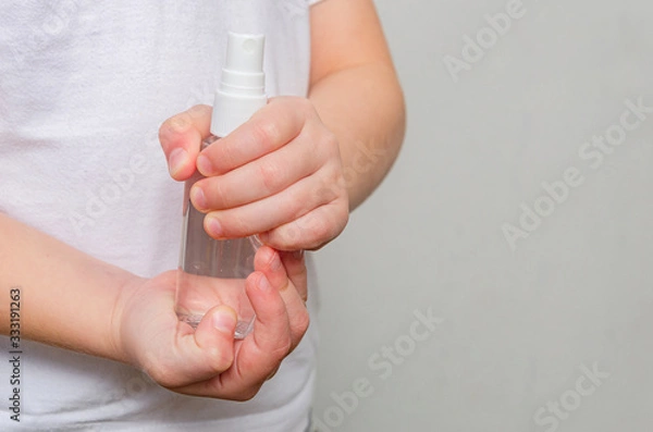Fototapeta Hands of a child of four years holding a bottle with a sanitizer on a gray background.