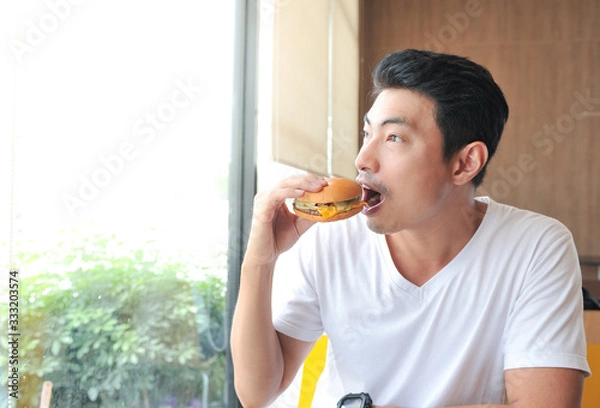 Fototapeta A man enjoy eating with her burger in hands,Asian man open his mouth for biting burger,Men eat burgers without knowing the danger of Junk Food.,Selective focus