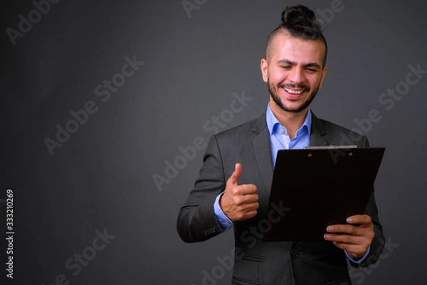 Obraz Happy bearded Turkish businessman in suit reading on clipboard and giving thumbs up