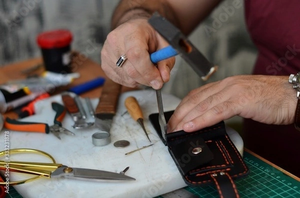 Obraz Handmade leather goods and handmade leather wallets lay on the table with crafting tools. Workflow in the workshop. Workflow in the workshop, close-up.