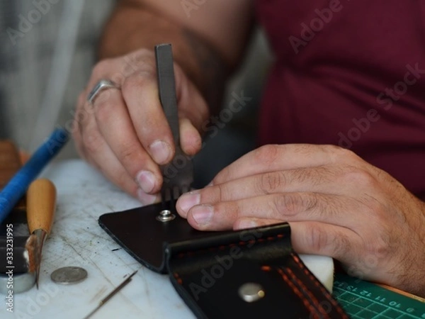 Obraz Leather goods master hands and handmade leather wallets lay on table with crafting tools. Workflow in the workshop. Workflow in the workshop, close-up.