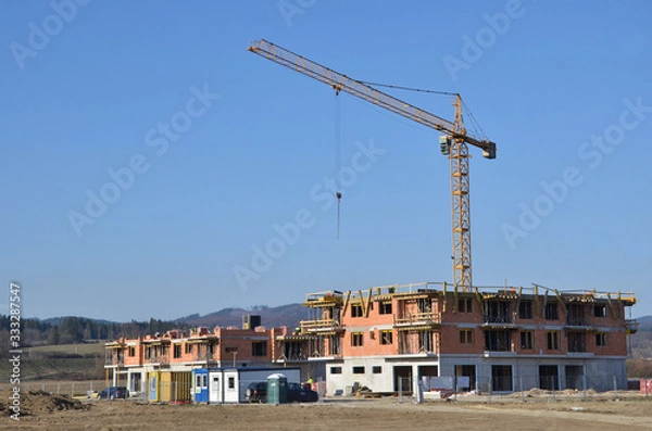 Fototapeta Two apartment houses under construction with yellow tower crane above construction site