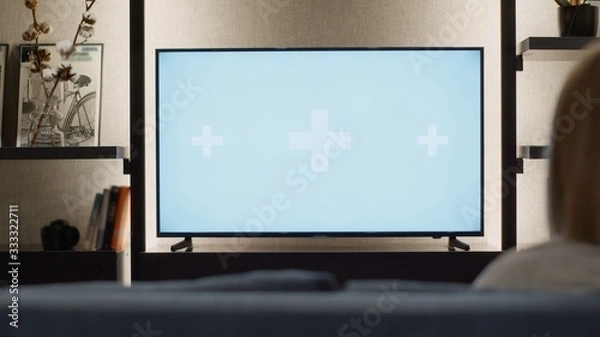 Fototapeta Over shoulder view of young woman relaxed at home watching television TV green white screen mock-up chroma key with track points. girl watches sports match, news, show or a movie