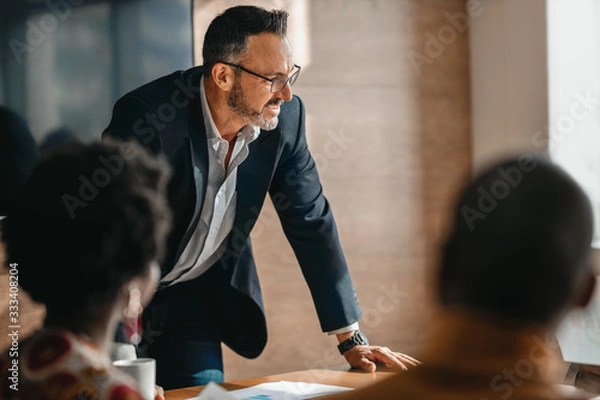 Fototapeta close up of businessman standing over boardroom table in front of South African coworkers during a diverse corporate meeting