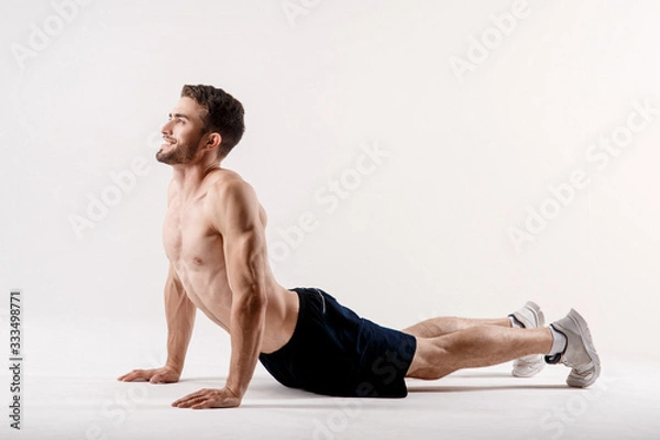 Fototapeta A man on a white background does an exercise on stretching his back. straight loin yoga exercise