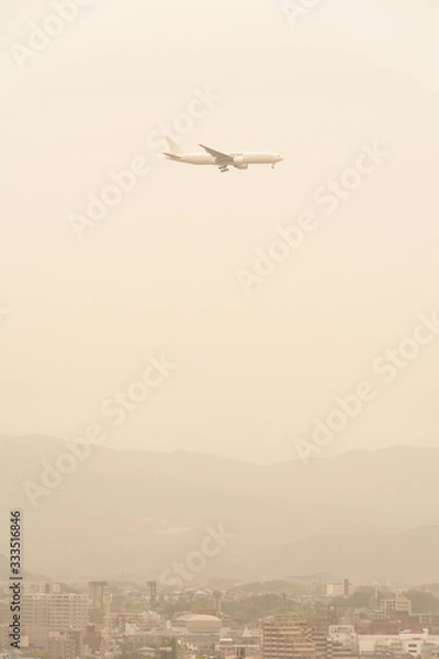 Obraz 黄砂に覆われた街並みを飛ぶ飛行機