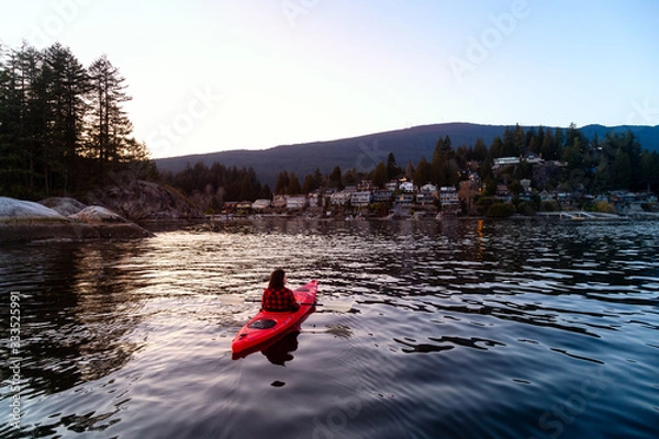 Fototapeta Adventurous Girl Paddling on a Bright Red Kayak in calm ocean water during a vibrant and colorful sunset. Taken in Indian Arm, Deep Cove, North Vancouver, British Columbia, Canada.